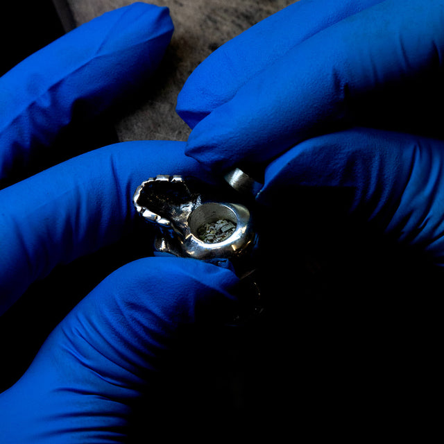 Ashes being placed inside a silver skull pendant by a jeweller.